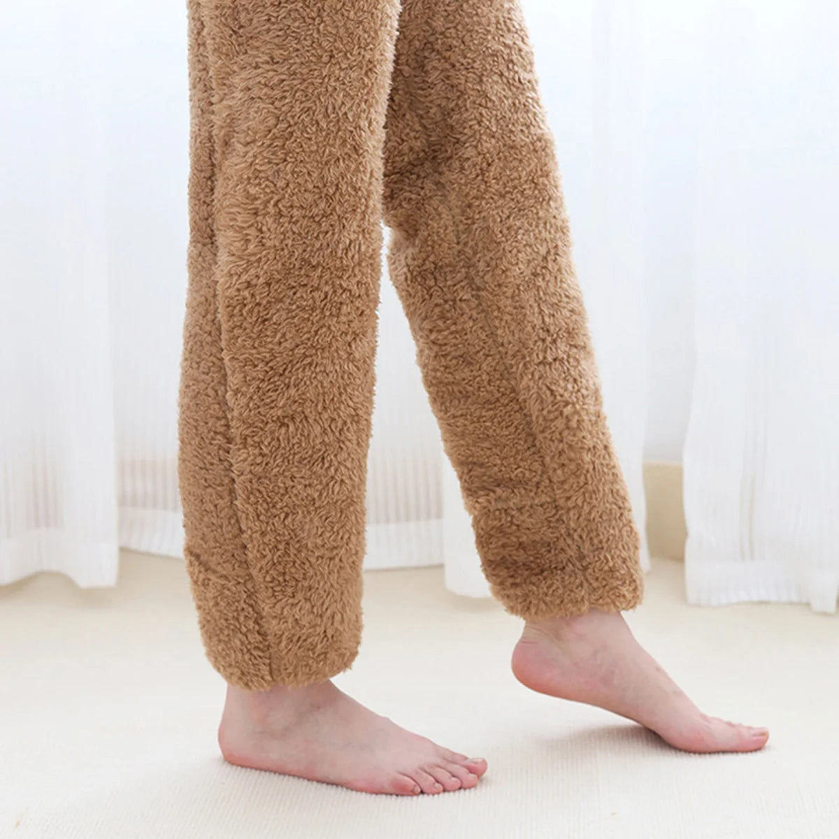 Brown fuzzy pants worn by a person on a light-colored floor with white curtains in the background.