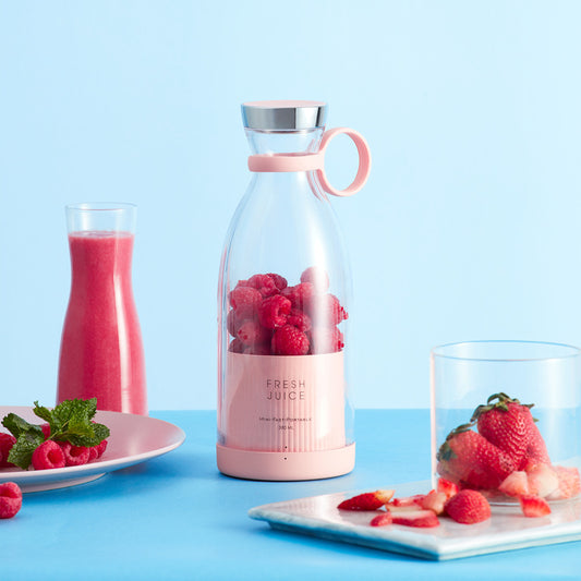 Pink juice bottle with raspberries, glass of pink juice, and plates of strawberries and raspberries on a blue background
