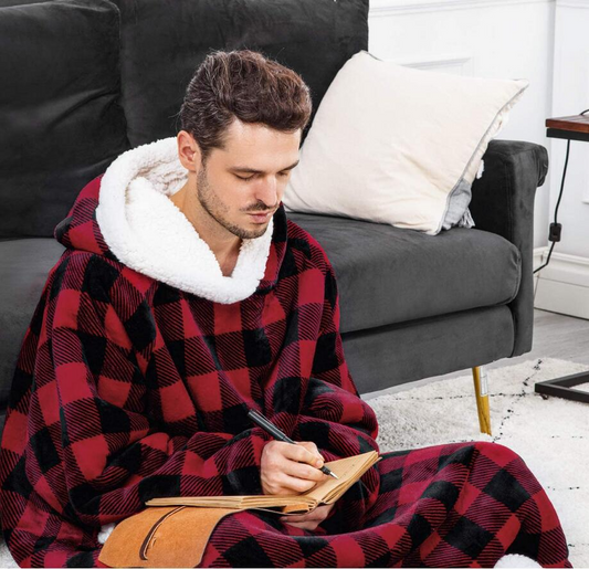 Man sitting on a couch wearing a red and black checkered blanket with white lining, writing in a notebook.