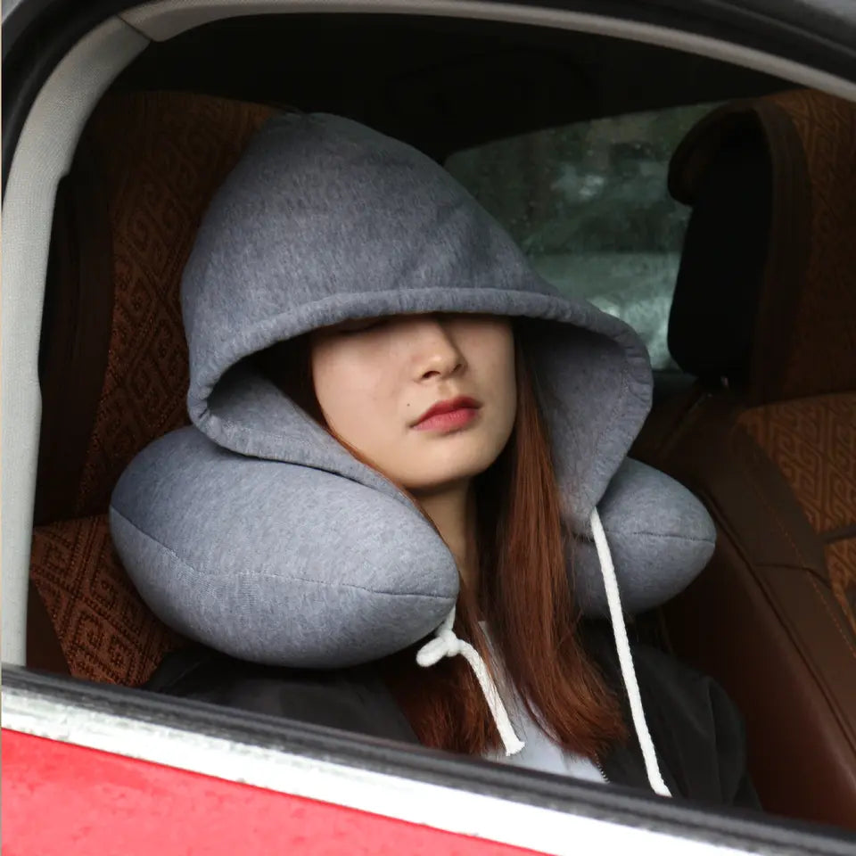 Person wearing a gray hooded travel pillow inside a car.