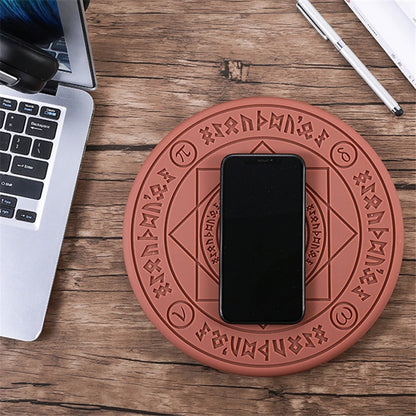 Red circular coaster with engraved symbols on a wooden surface with a phone and laptop.